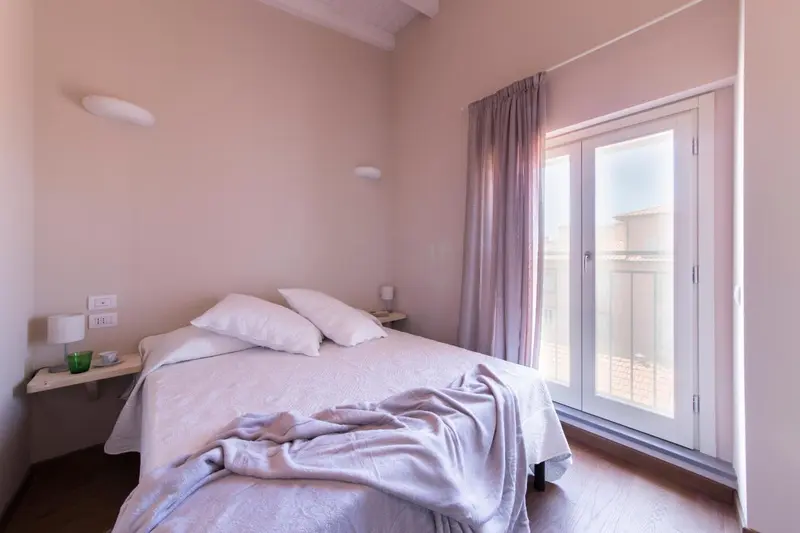 Une chambre lumineuse avec un lit double et une porte-fenêtre.