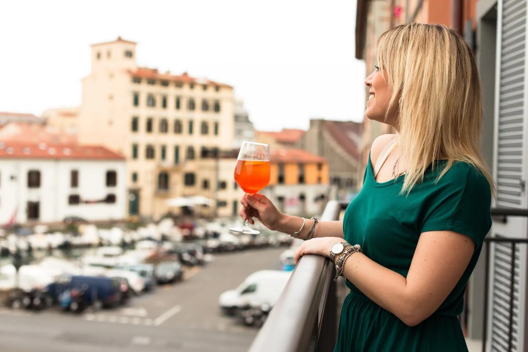 Une femme tient un verre sur un balcon avec vue sur la ville.