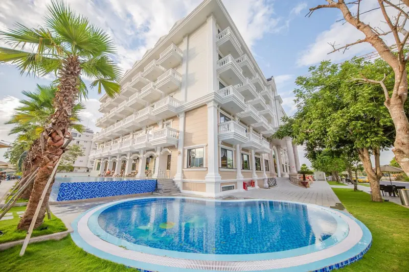 Bâtiment blanc à plusieurs étages avec une piscine circulaire au premier plan et des palmiers.