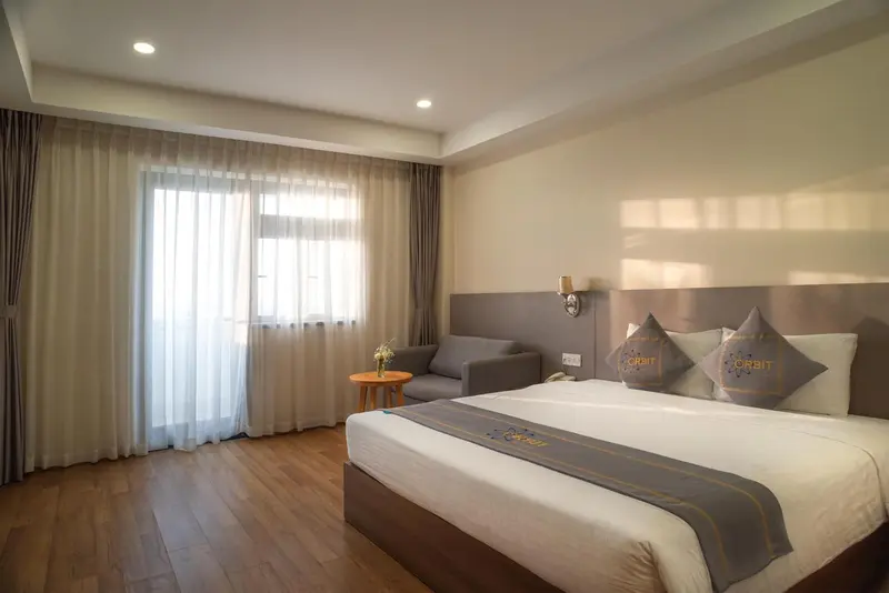 Chambre lumineuse avec un lit double et un coin salon près d'une fenêtre.