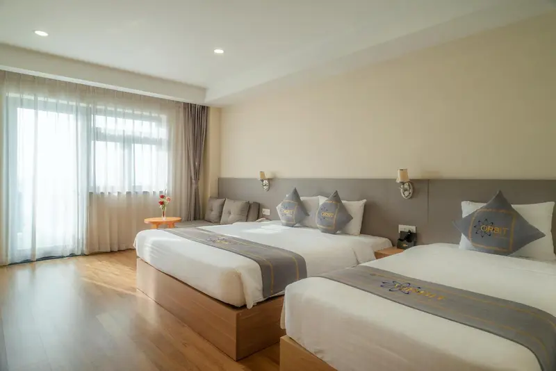 Chambre lumineuse avec deux lits simples et un canapé près d'une fenêtre.