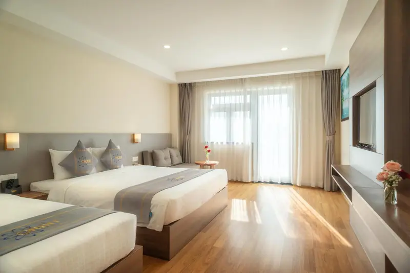 Chambre lumineuse avec deux lits et un canapé près d'une fenêtre.