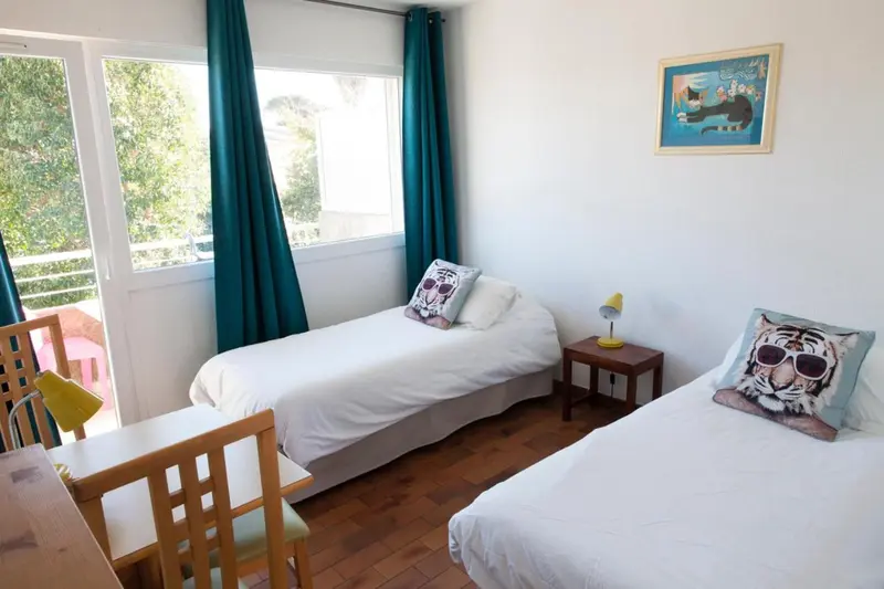 Une chambre lumineuse avec deux lits simples et une vue sur l'extérieur.