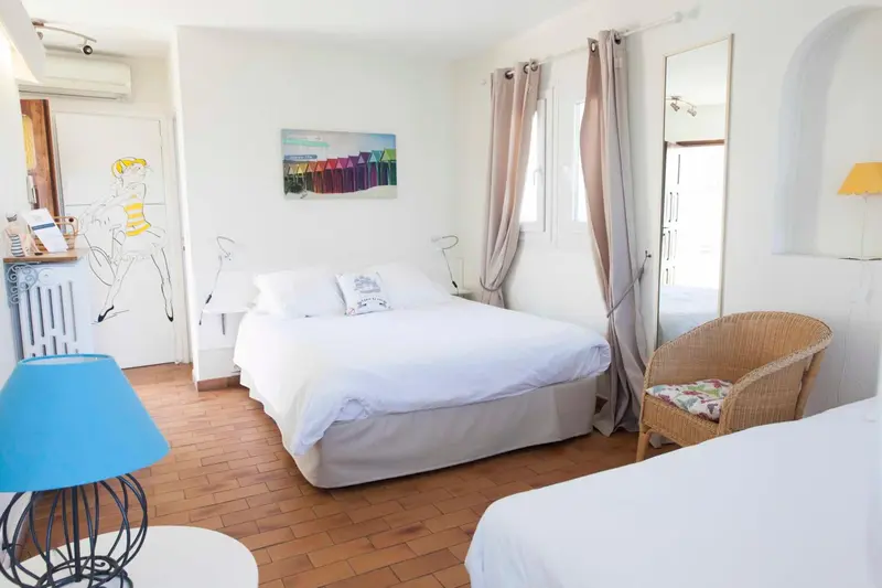 Une chambre lumineuse avec un lit double et un fauteuil en osier.