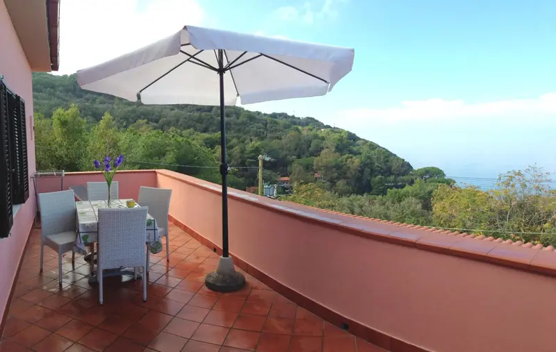 Terrasse avec table et chaises donnant sur un paysage verdoyant et la mer.