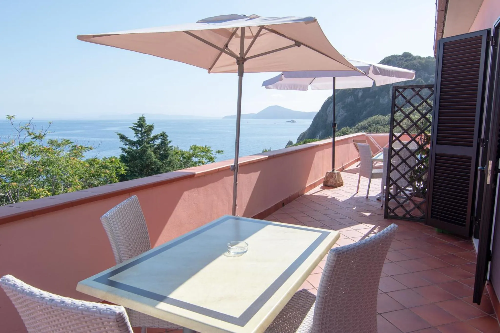 Terrasse avec table et chaises donnant sur la mer et les collines.