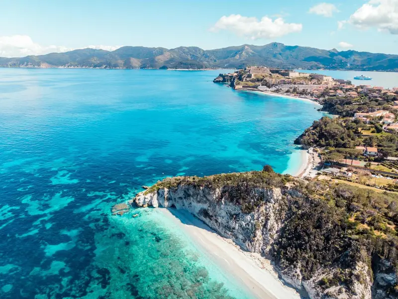 Vue aérienne d'une côte rocheuse avec une plage de sable fin et une mer turquoise.