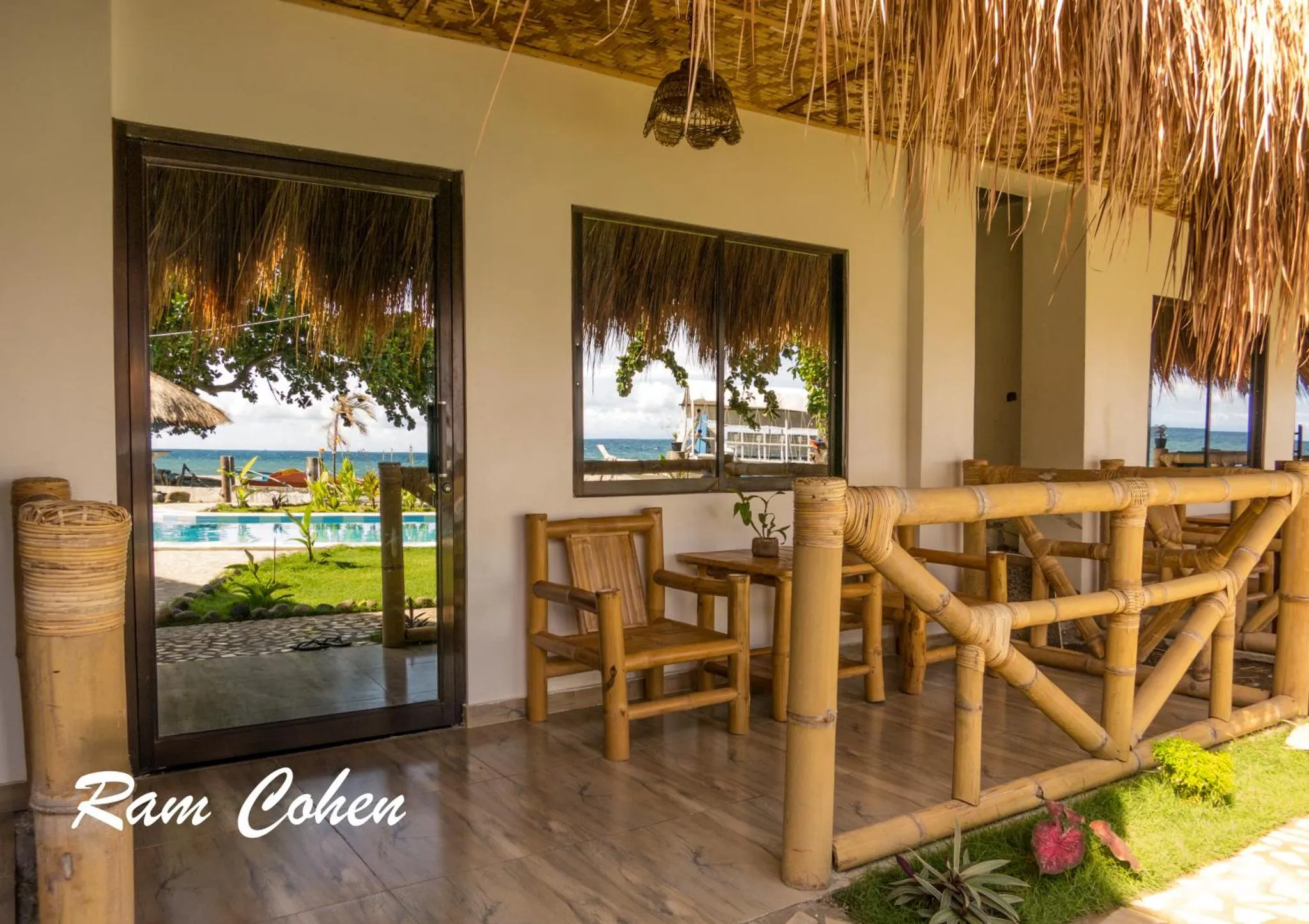 Terrasse ombragée avec mobilier en bambou donnant sur une piscine et la mer.