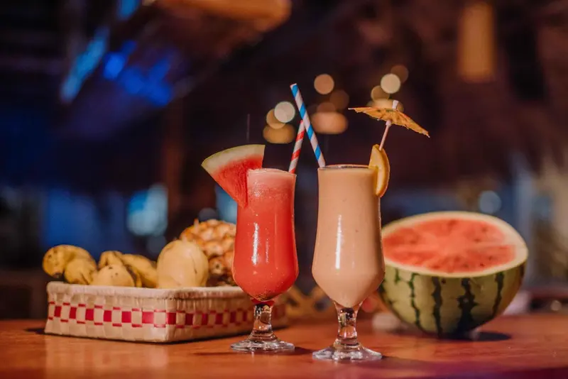 Deux cocktails colorés et des fruits frais sont présentés sur une table en bois.