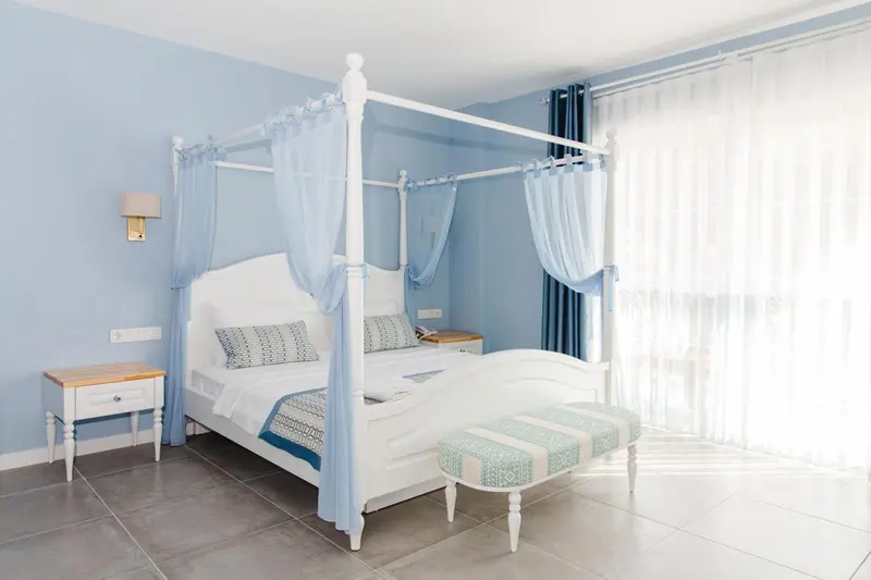 Une chambre lumineuse avec un lit à baldaquin blanc et des rideaux vaporeux.
