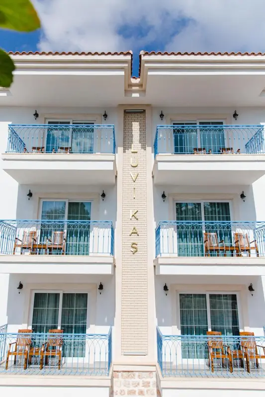 Façade d'un bâtiment blanc à deux étages avec des balcons bleus et des chaises en osier.