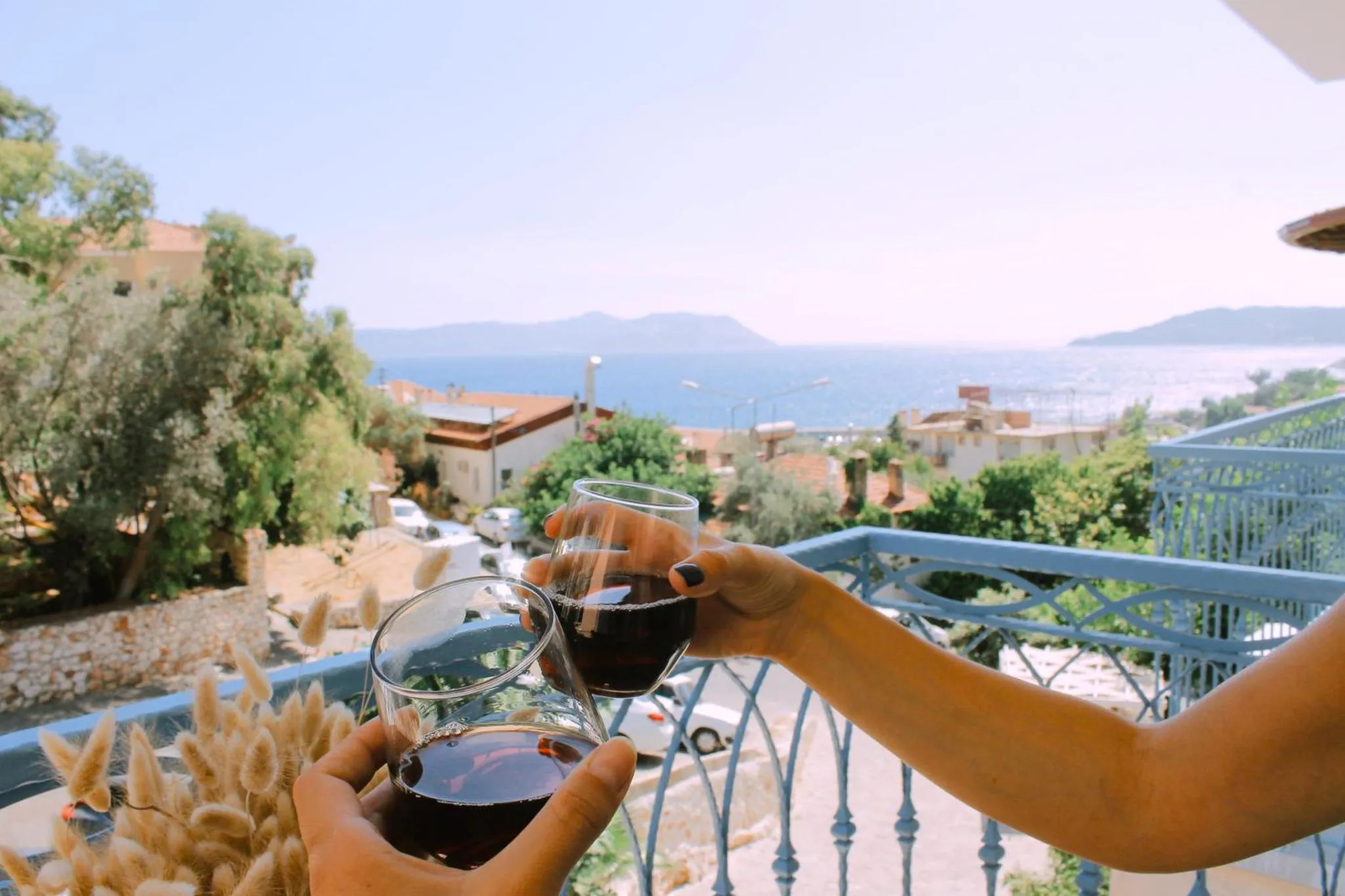 Deux verres de vin rouge sont tenus sur une terrasse ensoleillée avec vue sur la mer.