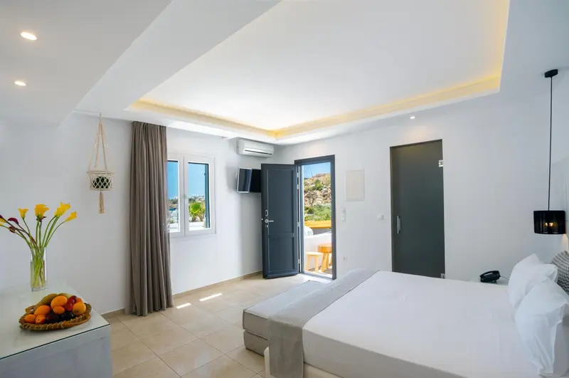 Une chambre lumineuse avec un grand lit et une porte-fenêtre ouverte sur une vue extérieure.