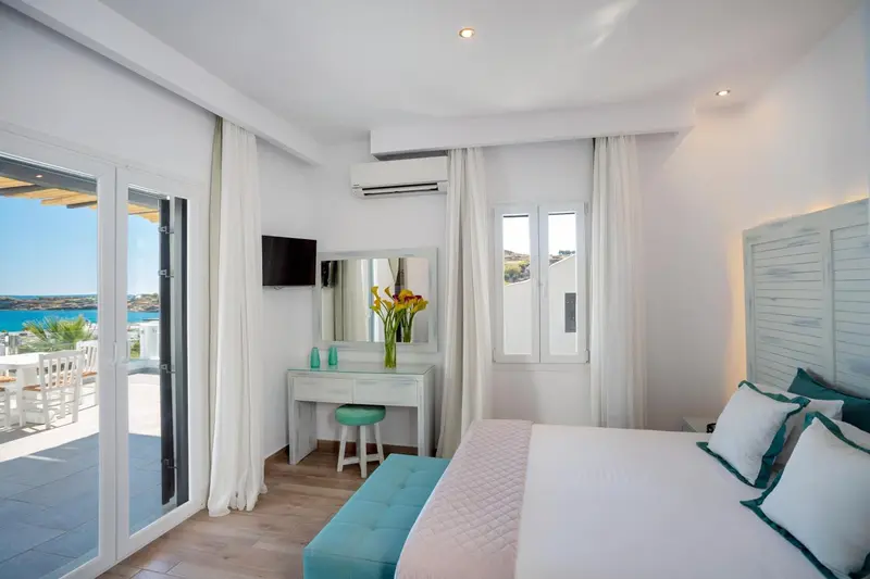 Chambre lumineuse avec un lit blanc et une vue sur la mer.