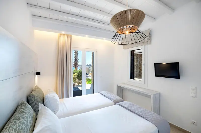 Chambre lumineuse avec deux lits simples et une vue sur l'extérieur.