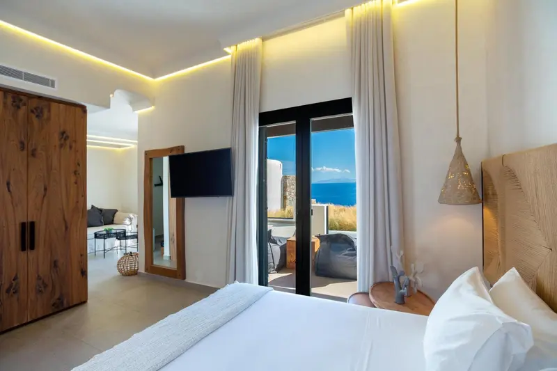 Une chambre lumineuse avec un lit fait et une vue sur la mer par une baie vitrée.