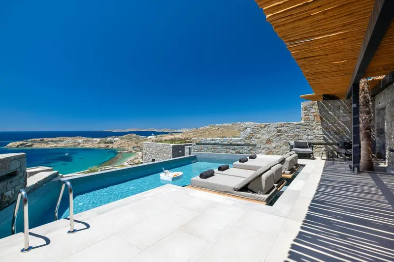 Terrasse avec transats et piscine à débordement offrant une vue sur la mer.