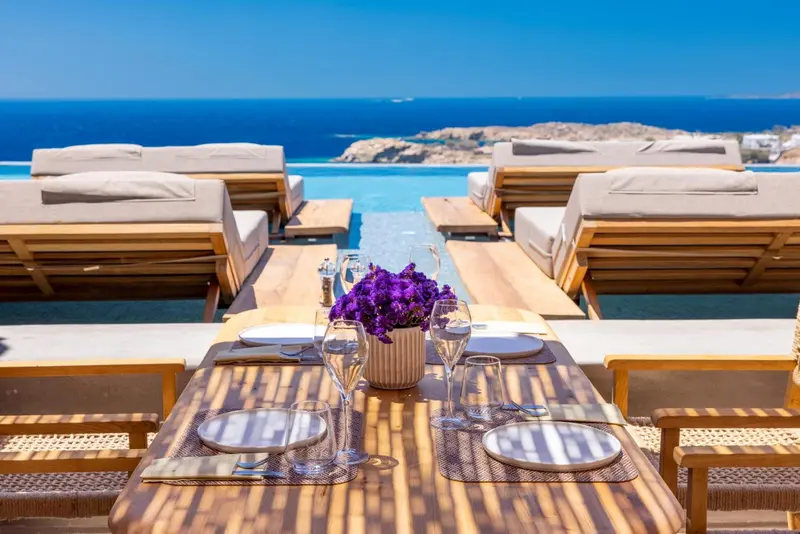 Tables et chaises longues disposées au bord d'une piscine à débordement avec vue sur la mer.