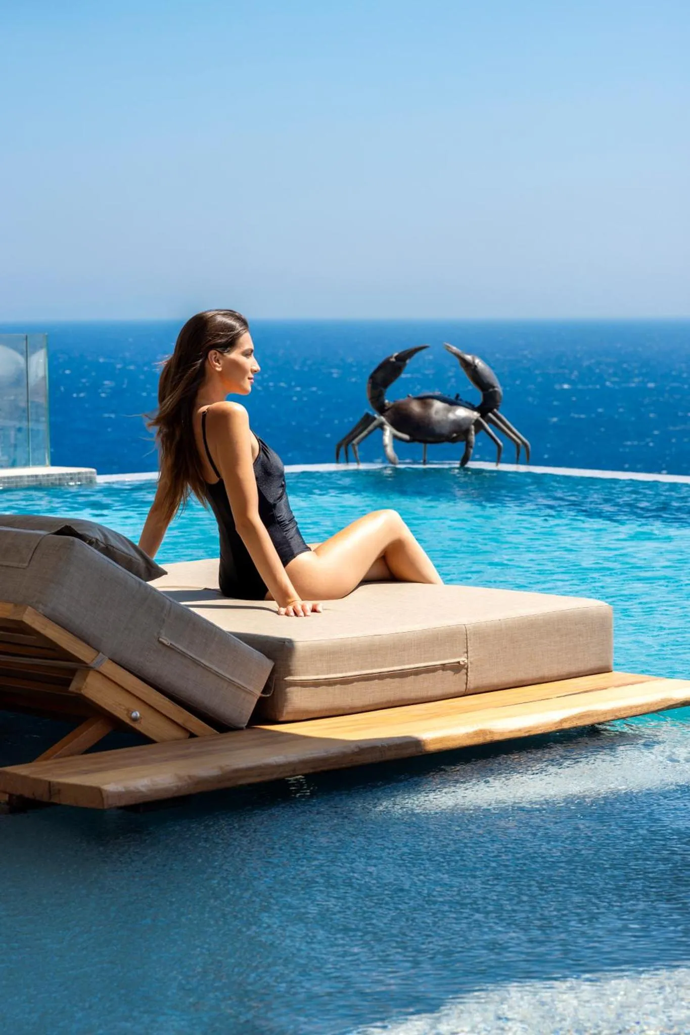 Une femme se détend au bord d'une piscine à débordement avec vue sur la mer.