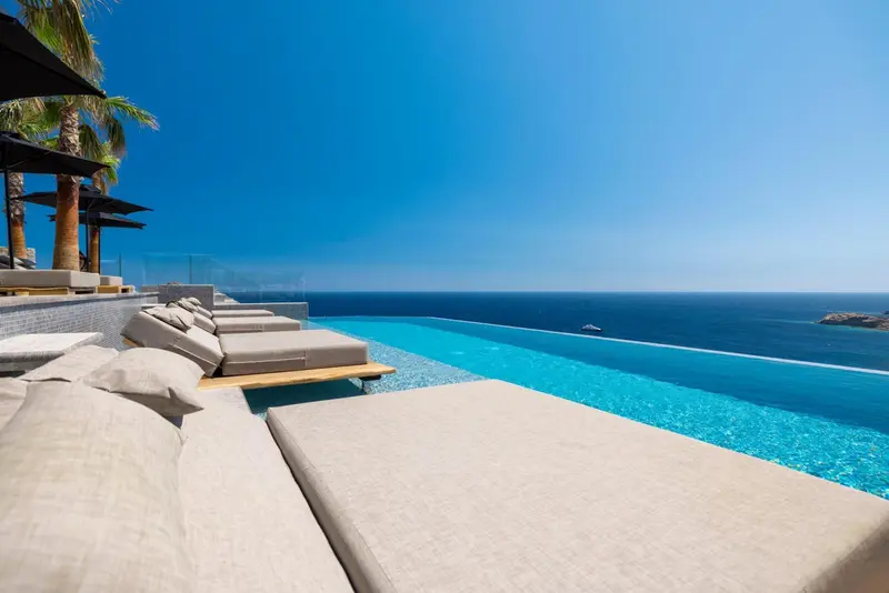 Transats et coussins au bord d'une piscine à débordement avec vue sur la mer.