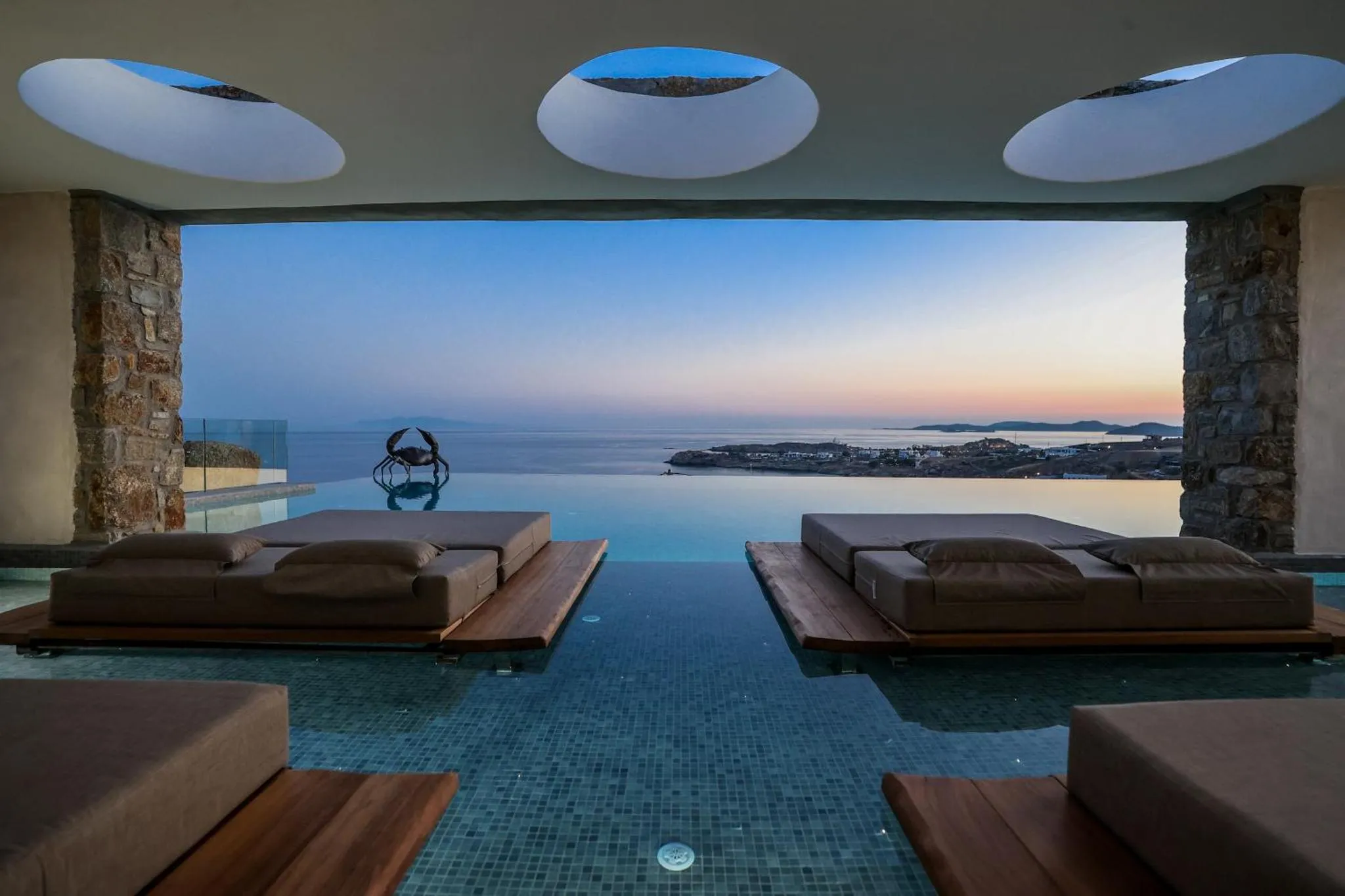 Deux transats sont posés sur une terrasse au bord d'une piscine à débordement avec vue sur la mer.