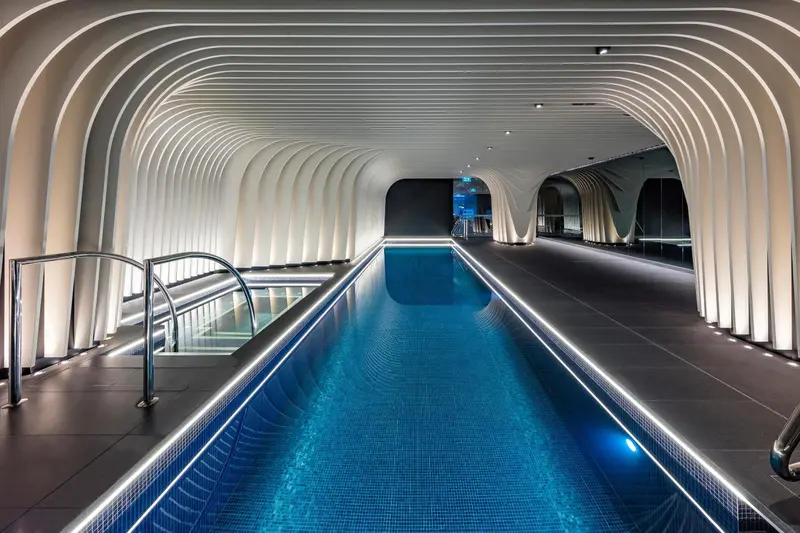 Une piscine intérieure rectangulaire est illuminée par un éclairage indirect et des leds bleues.