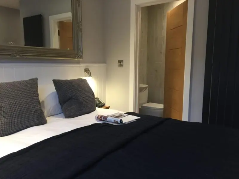 Une chambre avec un lit recouvert d'une couverture sombre et un miroir décoratif.
