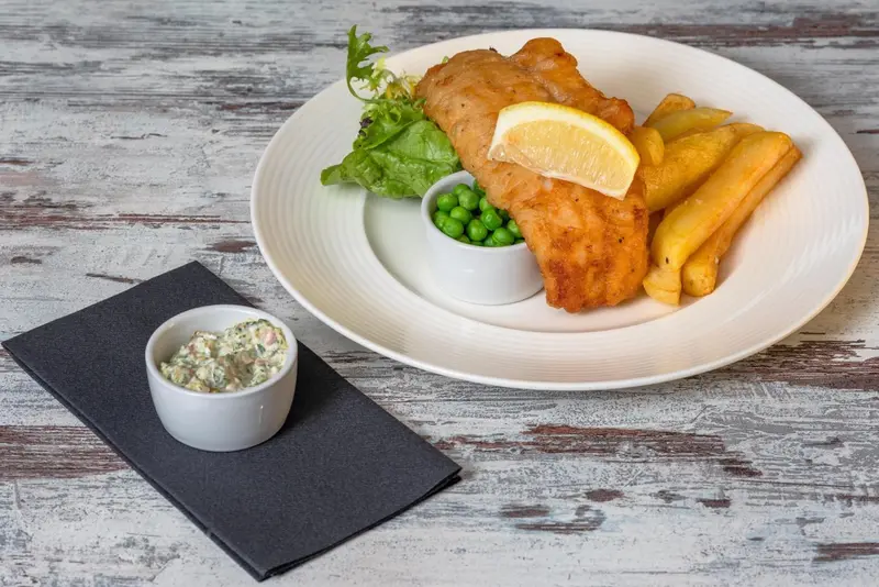 Assiette de poisson pané servi avec des frites et des petits pois.
