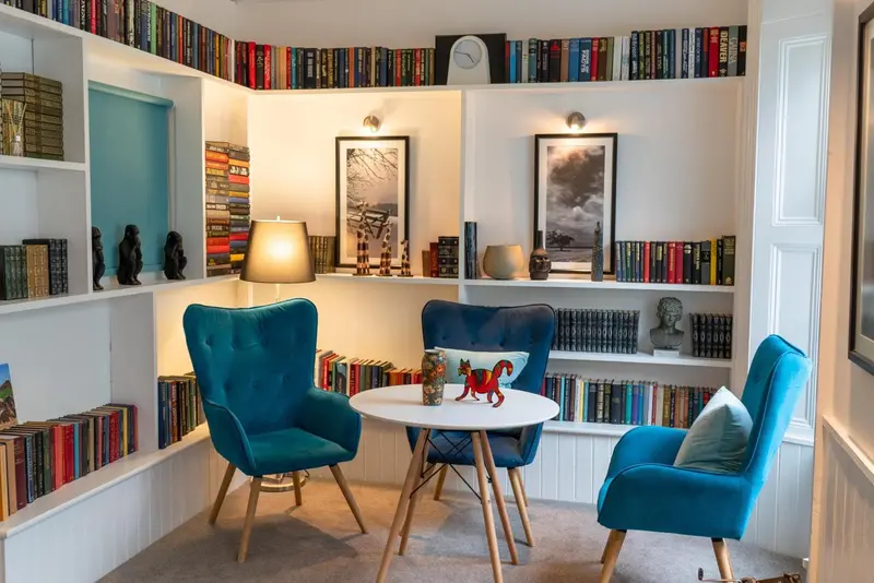 Un coin lecture confortable avec des fauteuils bleus et des étagères remplies de livres.