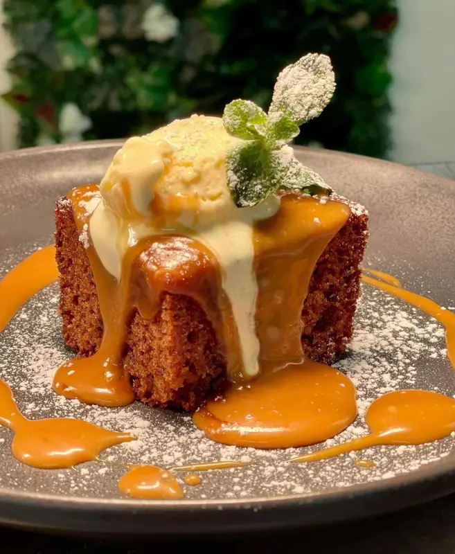 Une part de gâteau au caramel nappée de sauce, décorée de menthe et de sucre glace.