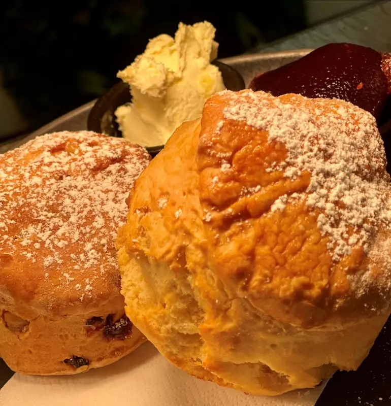 Deux scones recouverts de sucre glace accompagnés d'une crème et d'une confiture.