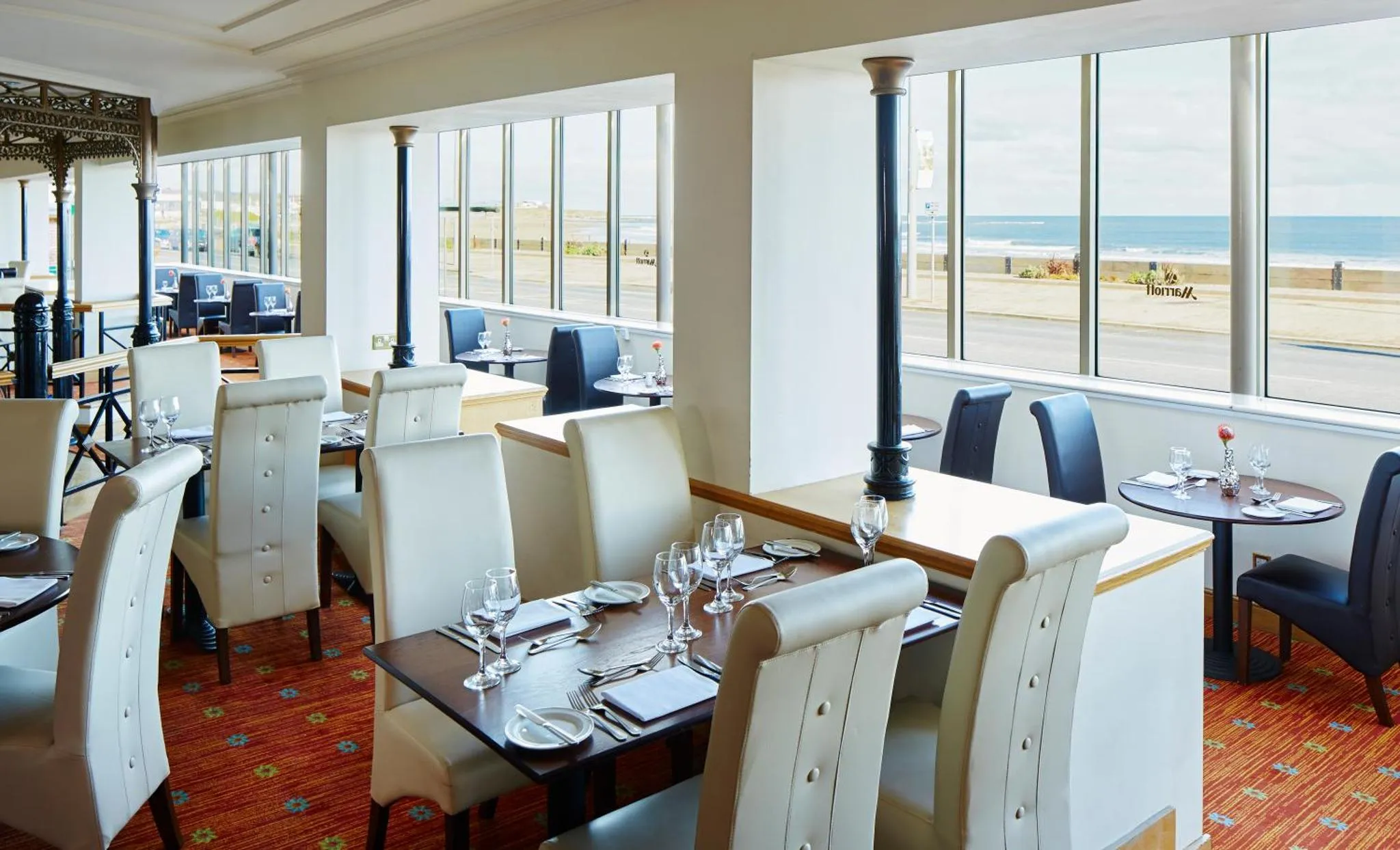 Une salle de restaurant lumineuse avec des tables dressées face à la mer.