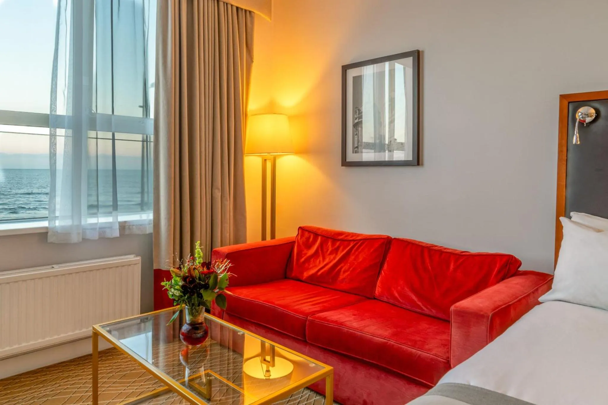 Un canapé rouge vif se trouve devant une grande fenêtre avec vue sur la mer.