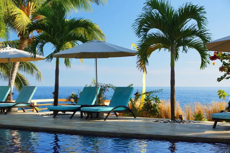 Transats bleus alignés au bord d'une piscine avec vue sur la mer.