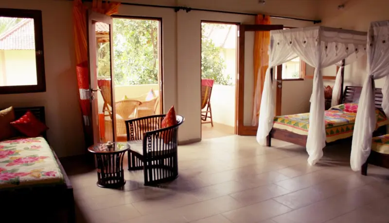 Une chambre lumineuse avec un lit à baldaquin et un coin salon donnant sur une terrasse.