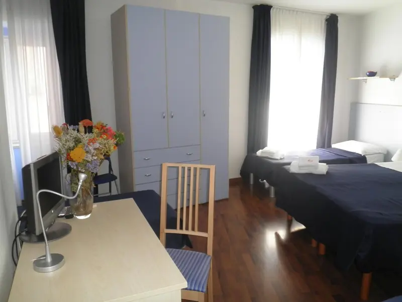 Une chambre lumineuse avec un bureau et un lit recouvert d'une couverture sombre.