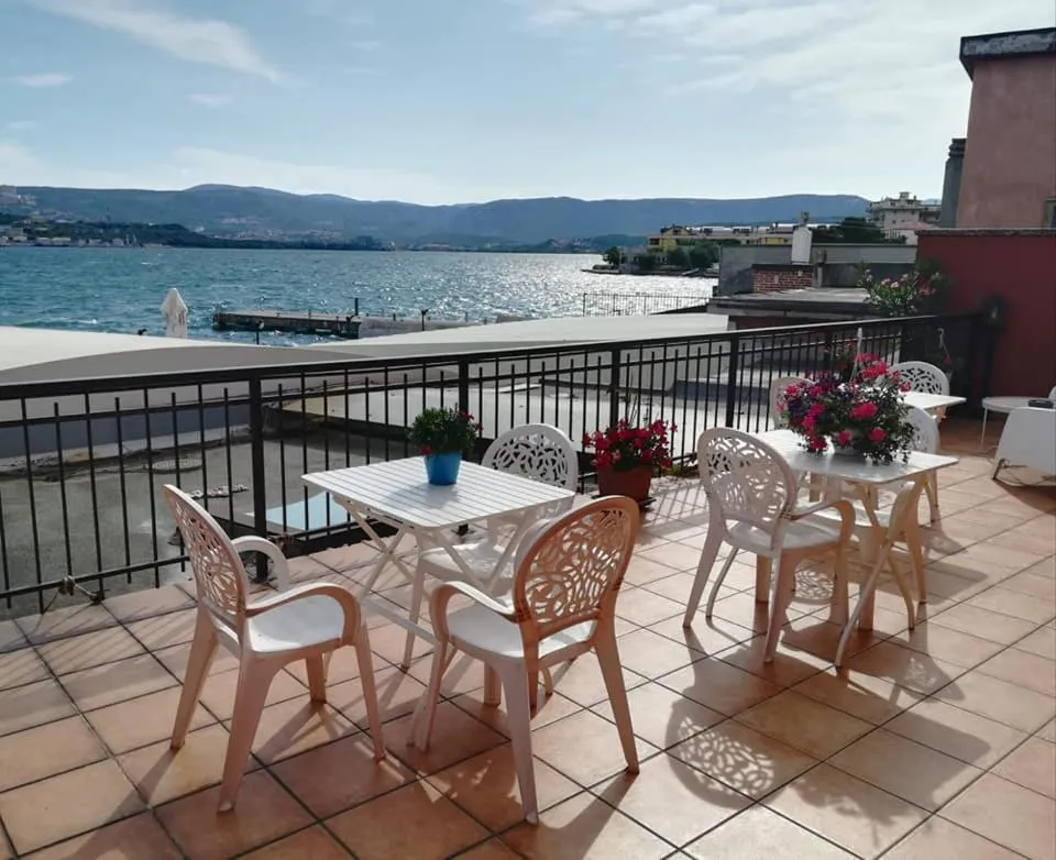 Terrasse ensoleillée avec tables et chaises donnant sur la mer et les montagnes.