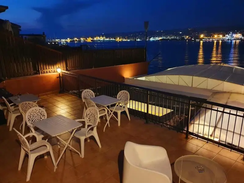 Terrasse lumineuse avec tables et chaises donnant sur une ville côtière illuminée.