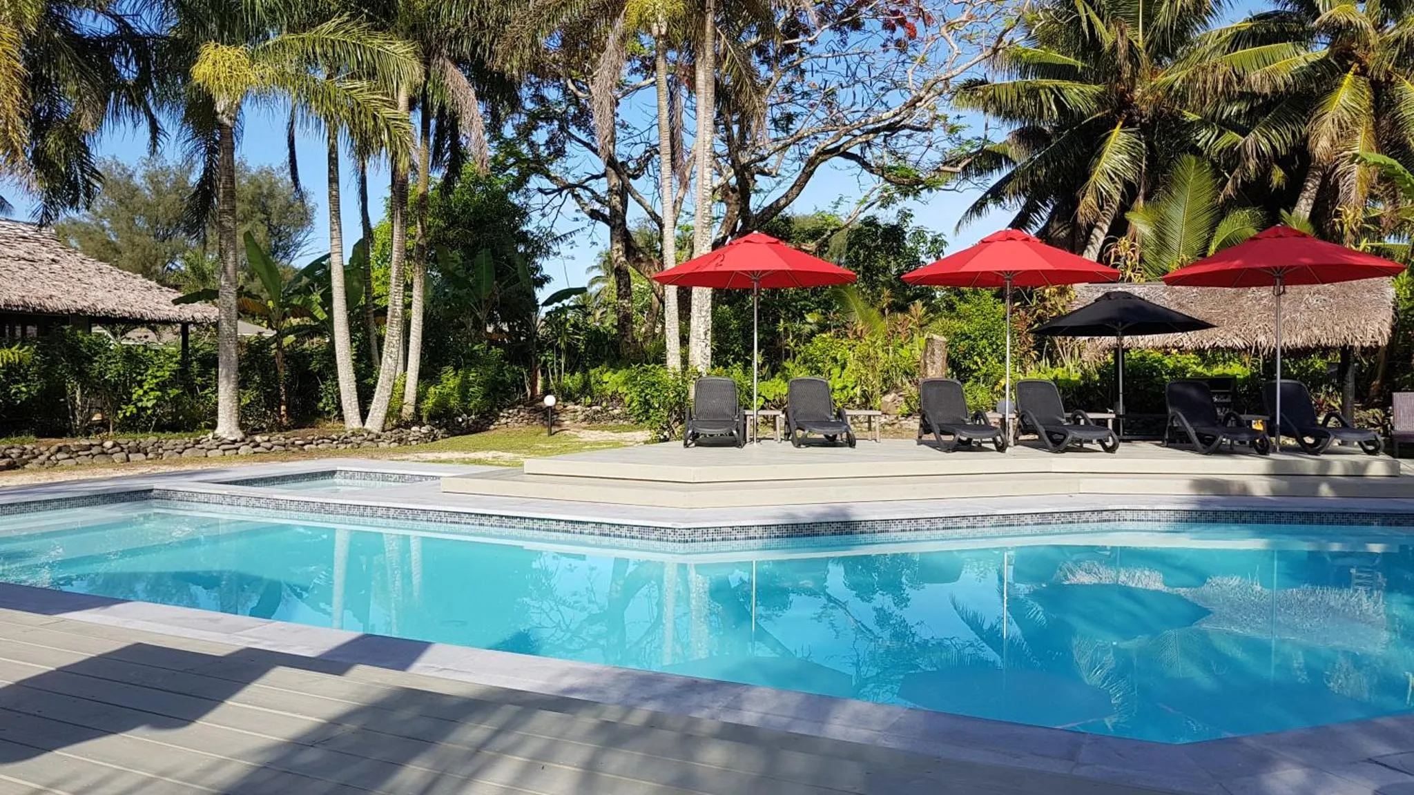 Une piscine bordée d'une terrasse avec des transats et des parasols rouges.