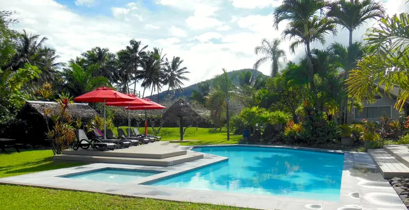Une piscine bordée de transats et de parasols, entourée d'une végétation luxuriante.