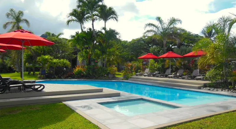 Une piscine rectangulaire bordée de transats rouges sous des parasols, entourée d'une végétation luxuriante.