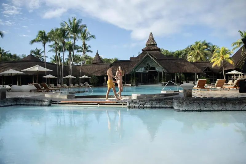 Une piscine bordée d'une terrasse avec des transats et des palmiers.