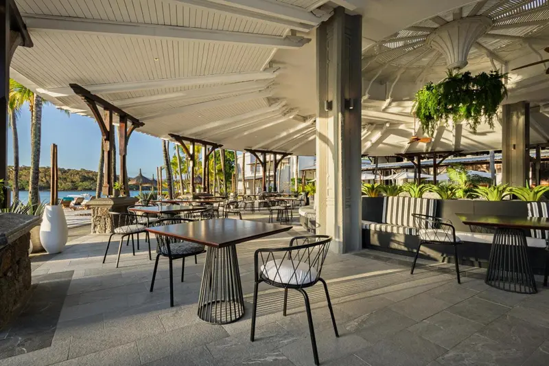Terrasse ombragée avec tables et chaises près d'une plage.