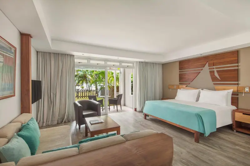 Une chambre lumineuse avec un lit double et un espace salon donnant sur une terrasse.