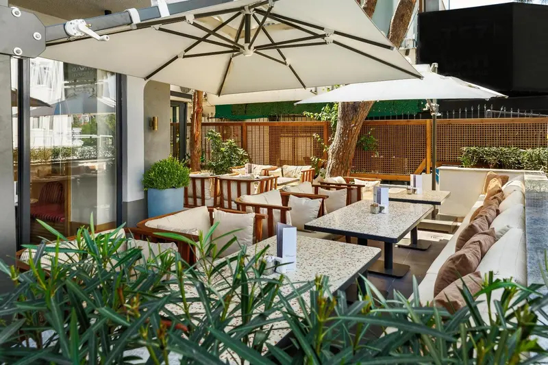 Terrasse ombragée avec tables et chaises pour les repas.