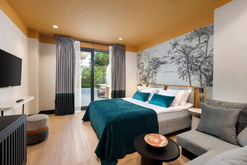 Chambre lumineuse avec un lit recouvert d'une couverture turquoise et un canapé gris.