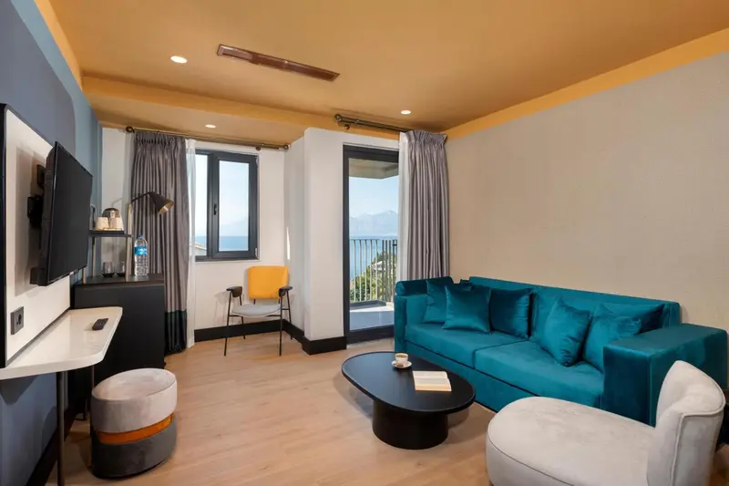 Un salon lumineux avec canapé turquoise et fauteuil jaune donne sur une vue mer.
