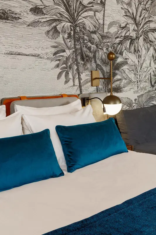 Un lit blanc avec des coussins turquoise est devant un mur décoré d'un motif tropical.