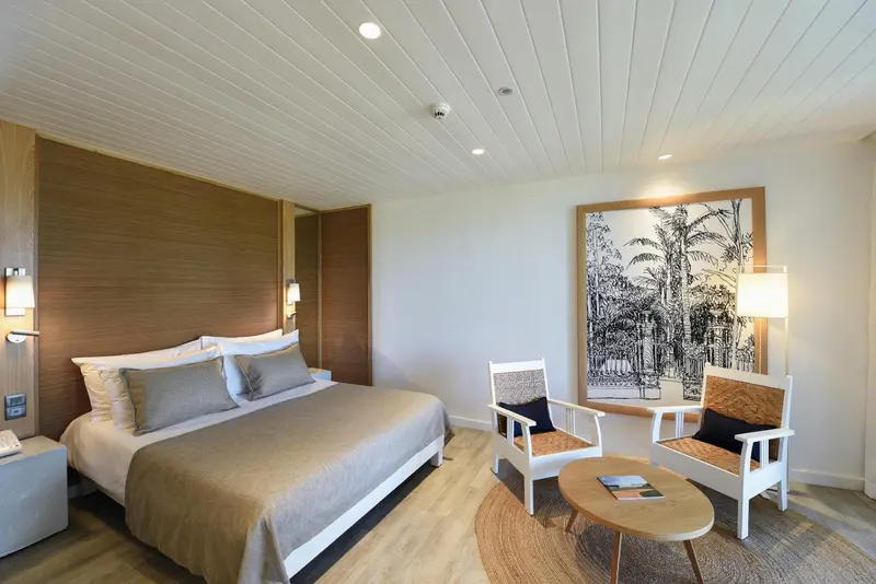 Une chambre lumineuse avec un lit double et deux fauteuils.