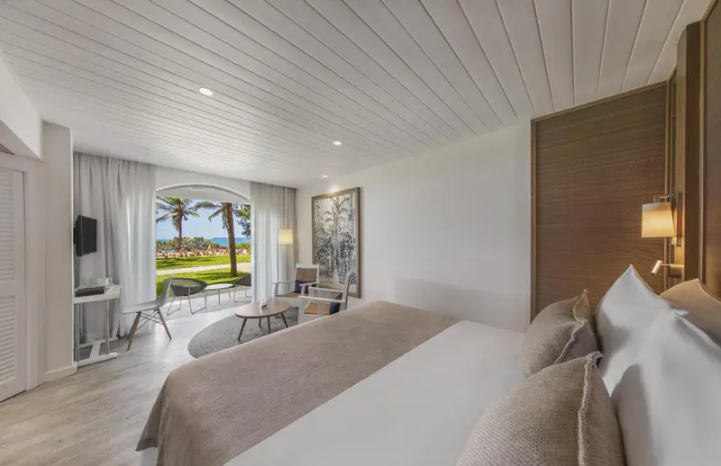 Une chambre lumineuse avec un lit double donnant sur une vue tropicale.